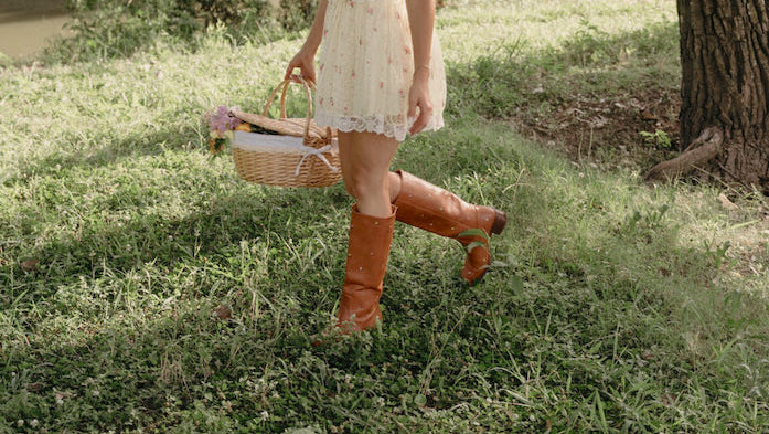 Woman in a white dress and orange boots standing in a grassy area with trees in the background